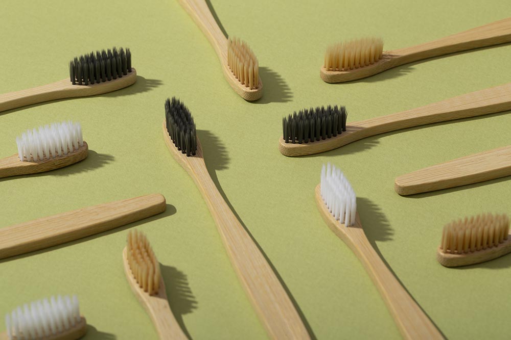 Деревянные зубные щетки с щетиной разного цвета и формы лежат горизонтально под углом друг к другу